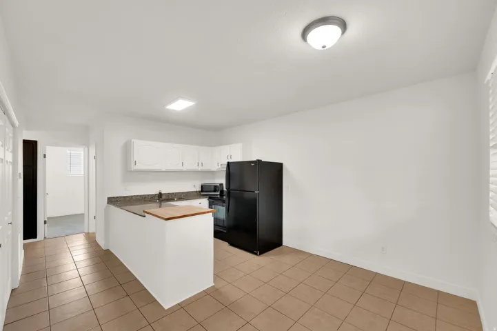 Kitchenette featuring white cabinetry, granite-style countertops, stainless steel sink, and tile flooring