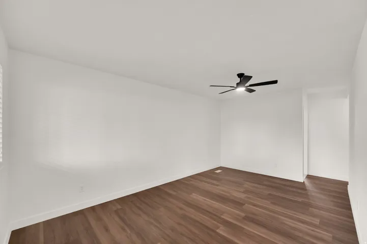Wood-finish flooring, white walls, and a black ceiling fan with integrated lighting