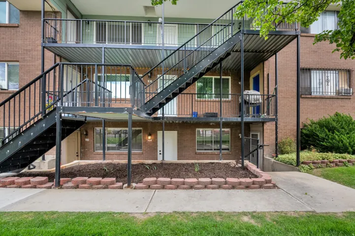 Brick exterior, multi-level metal staircase with railings, ground-level plantings with brick edging, concrete pathway, and mature landscaping