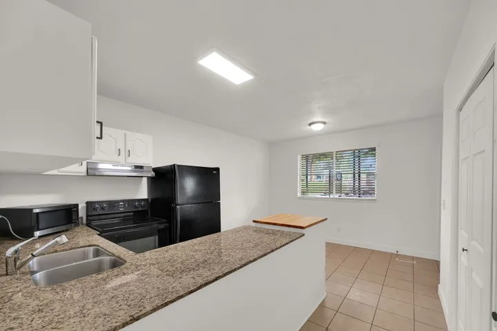 Kitchen featuring granite-finish countertops, stainless steel double basin sink, white cabinetry, integrated range hood, and tile flooring