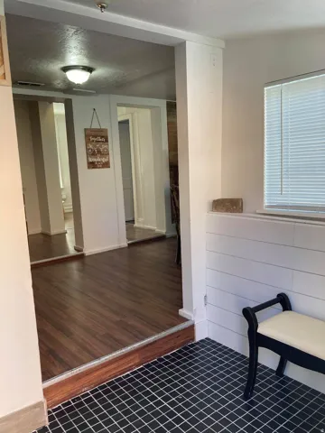 Black square tile flooring, wood-finish flooring, white shiplap wall paneling, and a window with blinds