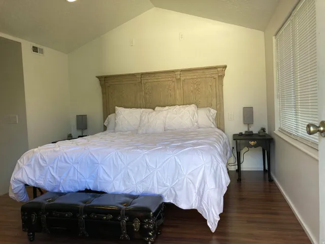 Vaulted ceiling with recessed lighting, wood-finish flooring, and window with blinds