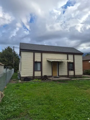 Pitched roof with dark shingles, horizontal siding, front entry with awning, concrete front stoop, and a chain-link fence