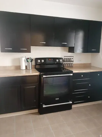 Black cabinetry with silver-tone hardware, light-toned countertops, tile flooring, and a black range