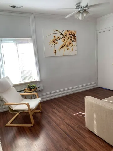 Wood-finish flooring, ceiling fan with integrated lighting, window with blinds, and white trim details