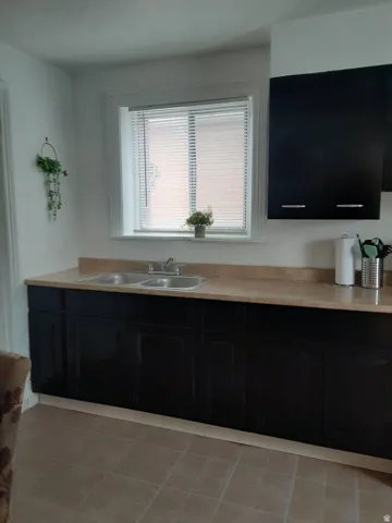Kitchen featuring dark cabinetry, light-toned countertops, a stainless steel double basin sink, and window with blinds