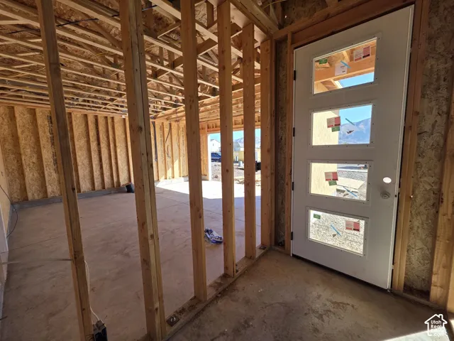 New construction framing with an unfinished concrete floor, exposed wooden studs, and a white entry door with four rectangular lites