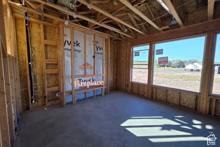 Framed construction featuring a fireplace rough-in, multiple windows, exposed wood ceiling joists, and a concrete floor