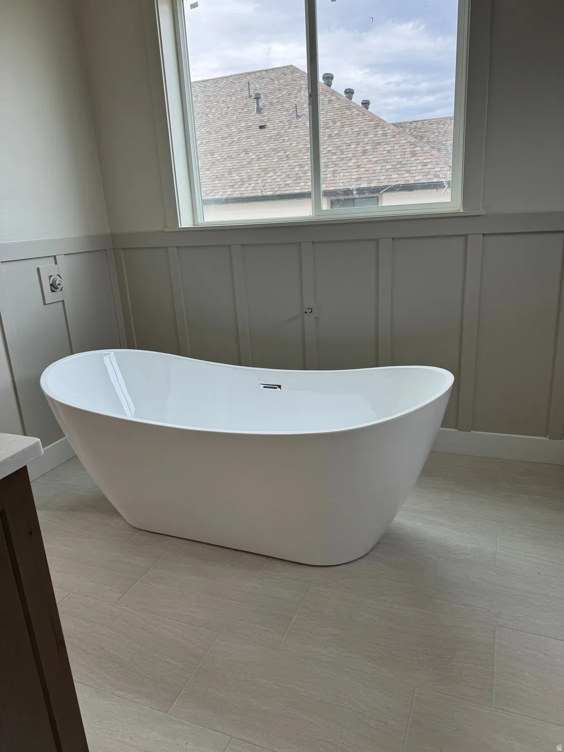 Freestanding soaking tub, board and batten wall paneling, large window, and tile flooring
