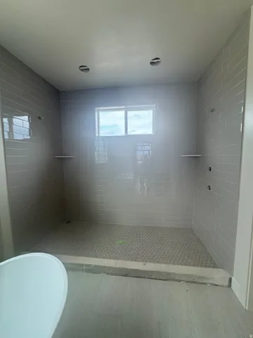 Expansive walk-in shower featuring light grey subway tile walls, a grey hexagon tile floor, and a window for natural light
