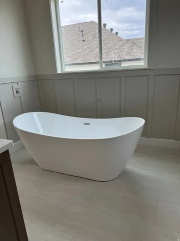 Freestanding soaking tub, board and batten wall paneling, large window, and tile flooring