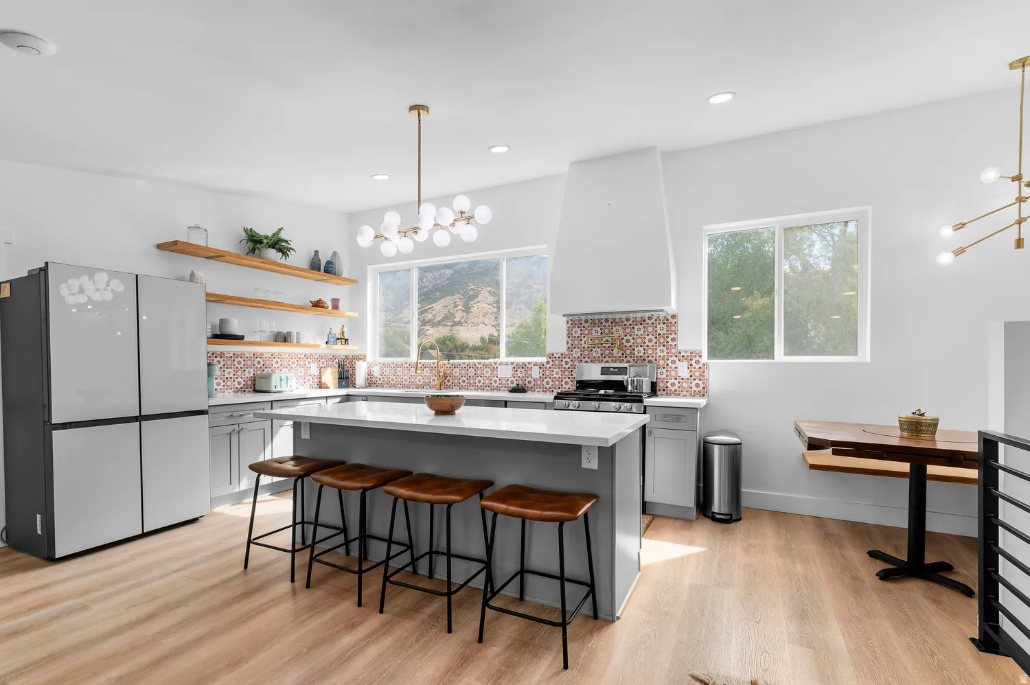 Guest house kitchen featuring wood-finish flooring, a central island with countertop seating, open shelving, a patterned tile backsplash, and stainless steel appliances