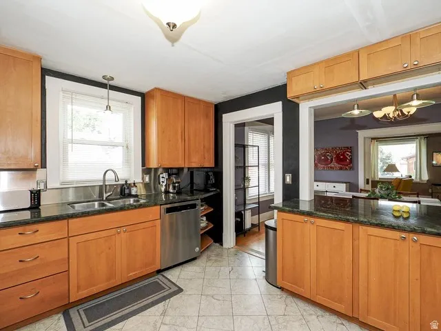 Kitchen featuring wood cabinetry, dark countertops, a stainless steel dishwasher, and a tile floor