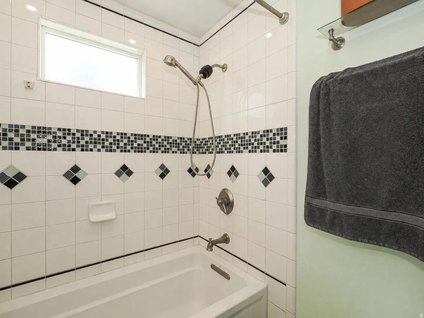 Built-in tub with white tile surround, mosaic accent tiling, and a frosted window