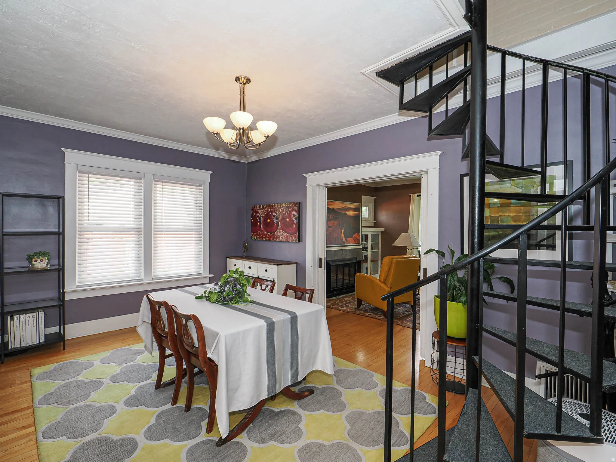 Hardwood flooring, two large windows with blinds, recessed archway, spiral staircase with metal railing, and a five-light chandelier