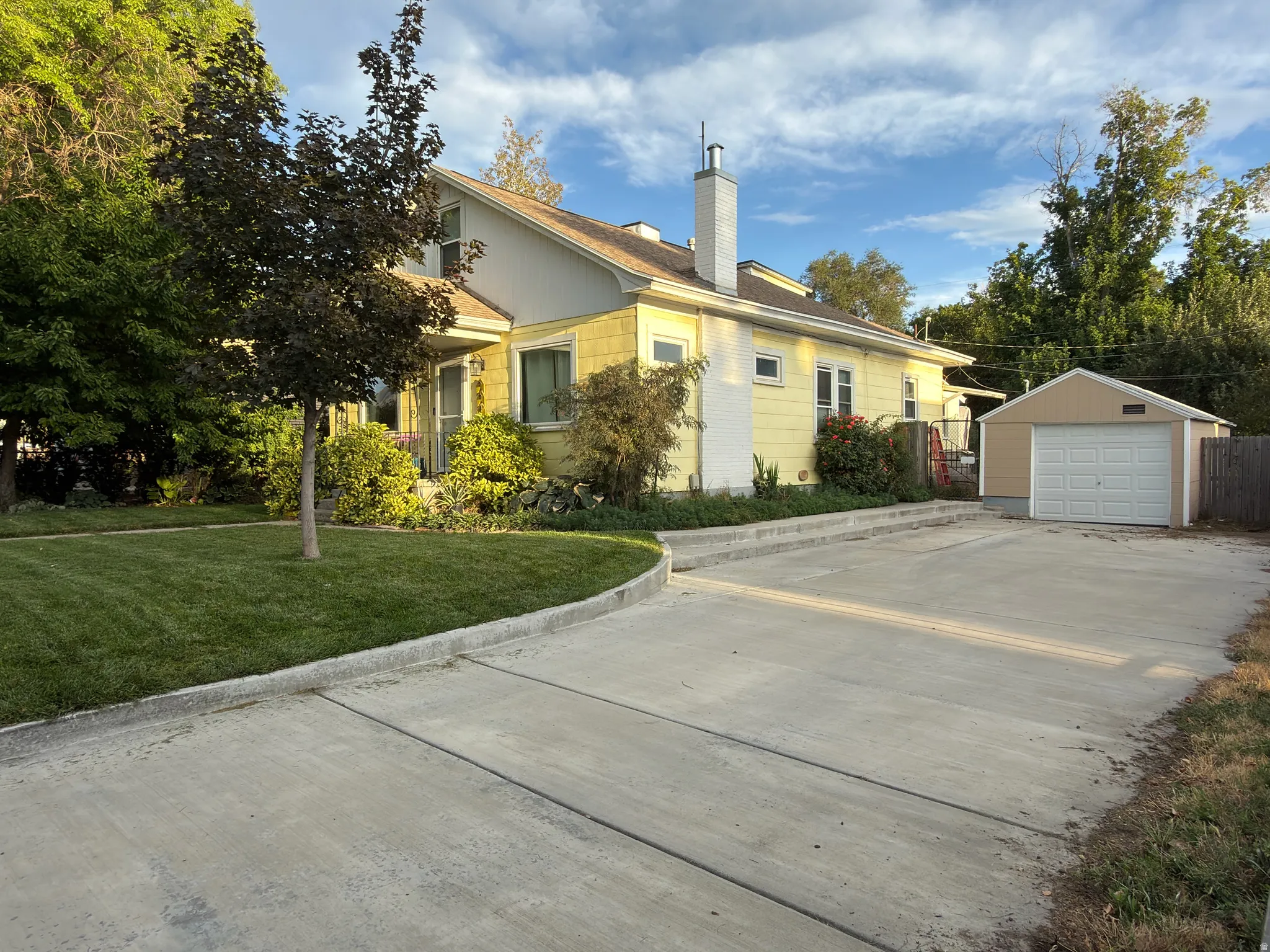 Spacious concrete driveway, single-car detached garage, mature trees, manicured lawn, and traditional exterior siding