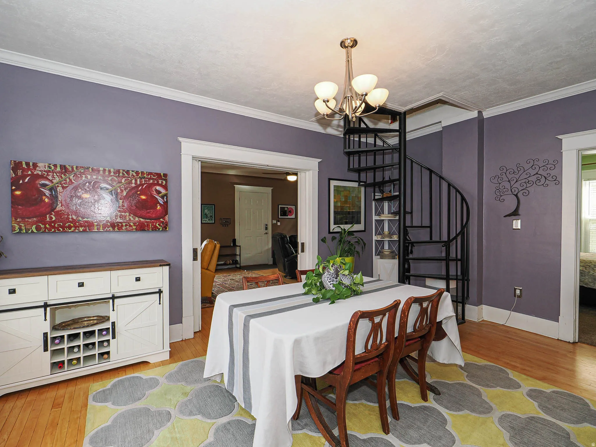 Hardwood flooring throughout, featuring a black spiral staircase, crown molding, and a chandelier with frosted glass shades