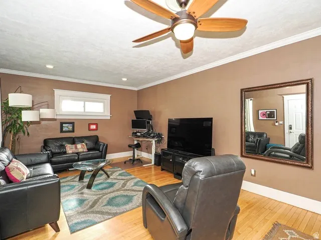 Hardwood flooring, crown molding, ceiling fan with integrated lighting, recessed lighting, and a white-framed window