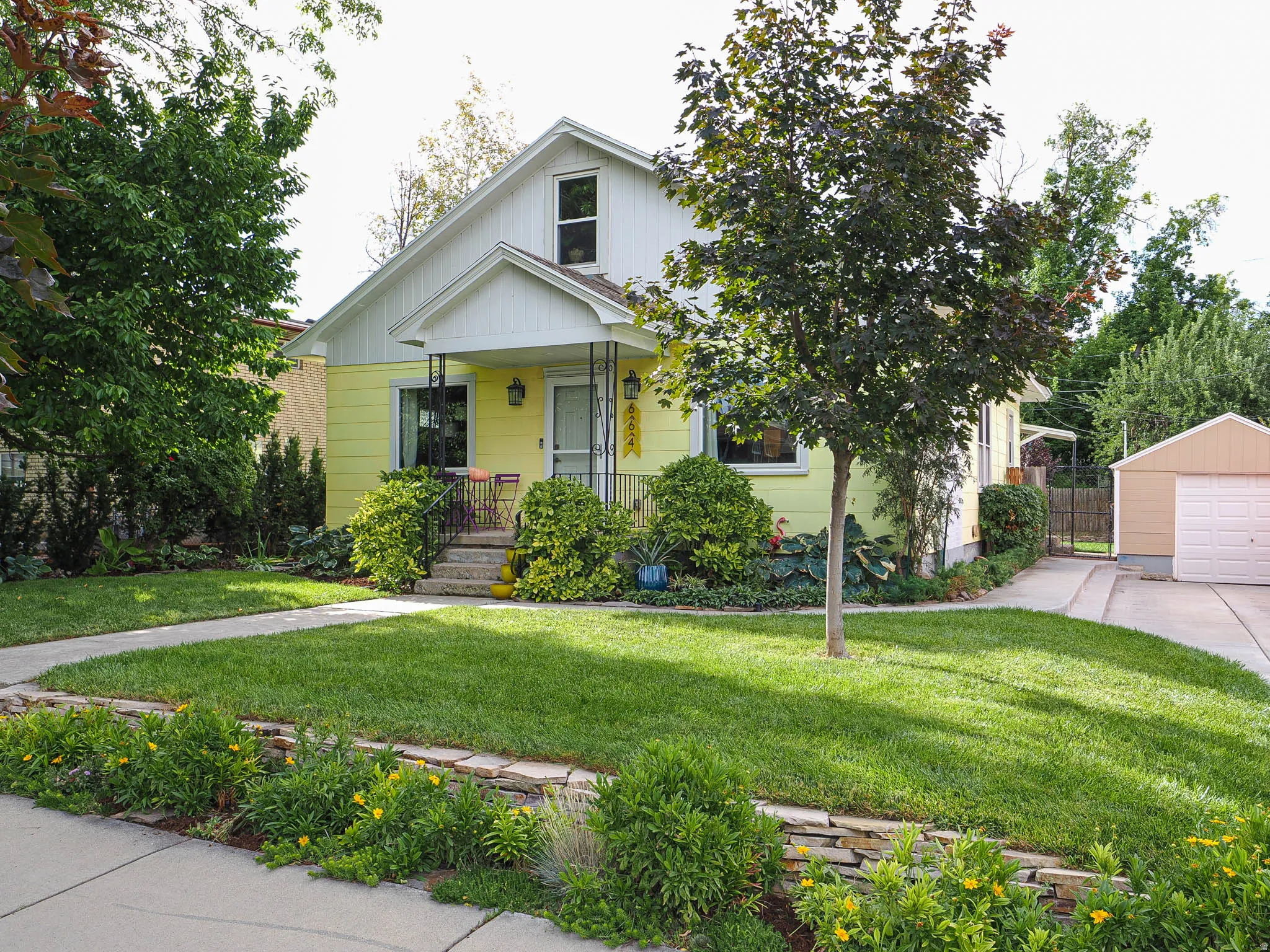 Yellow exterior with white trim, covered front porch, concrete pathway, stone retaining wall, and detached garage