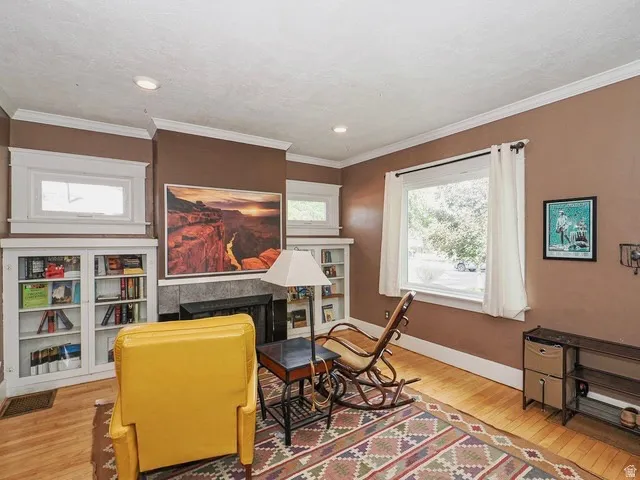 Hardwood flooring, recessed lighting, built-in shelving with glass doors, fireplace with stone surround, and crown molding