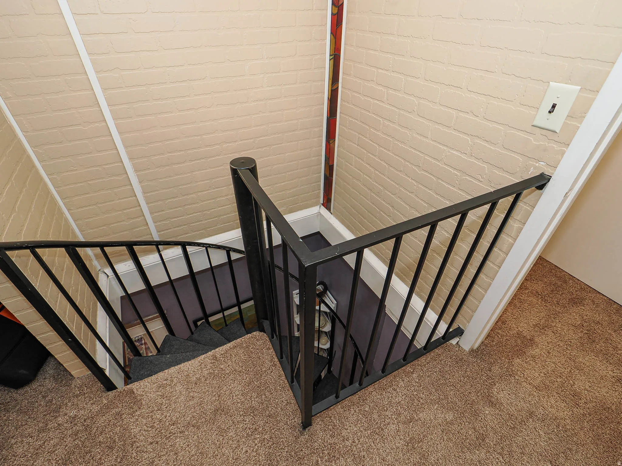 Spiral staircase with black wrought iron railing, textured wall finish, and carpeted stairs