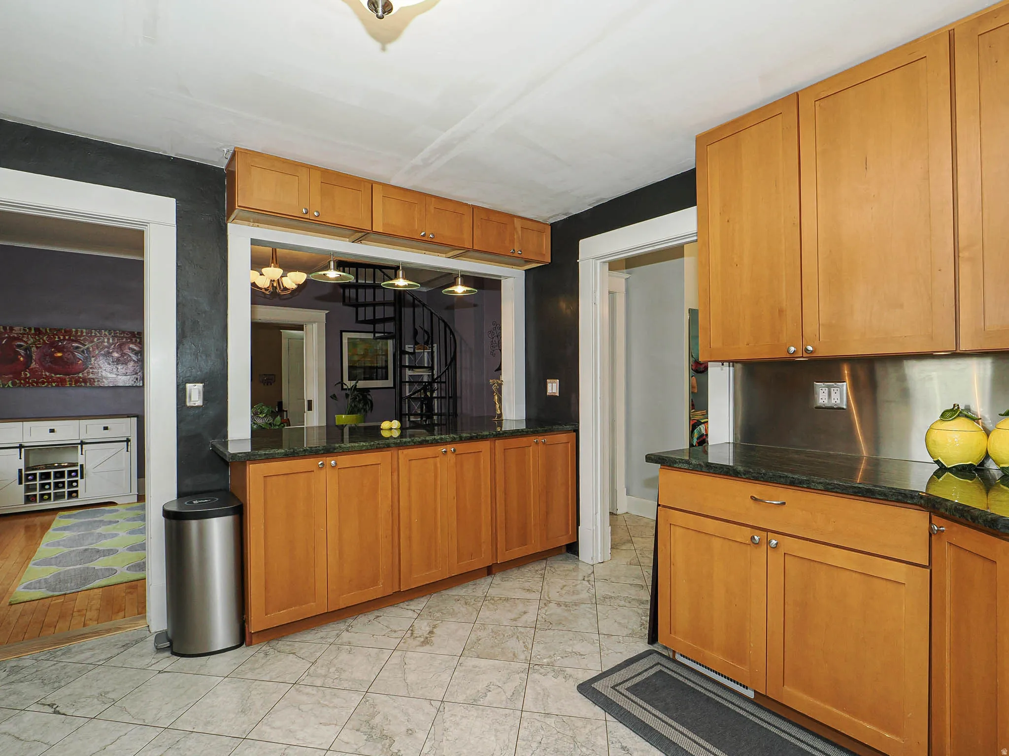 Kitchen featuring wood-finish cabinetry, dark countertops, tiled flooring, and a stainless steel backsplash