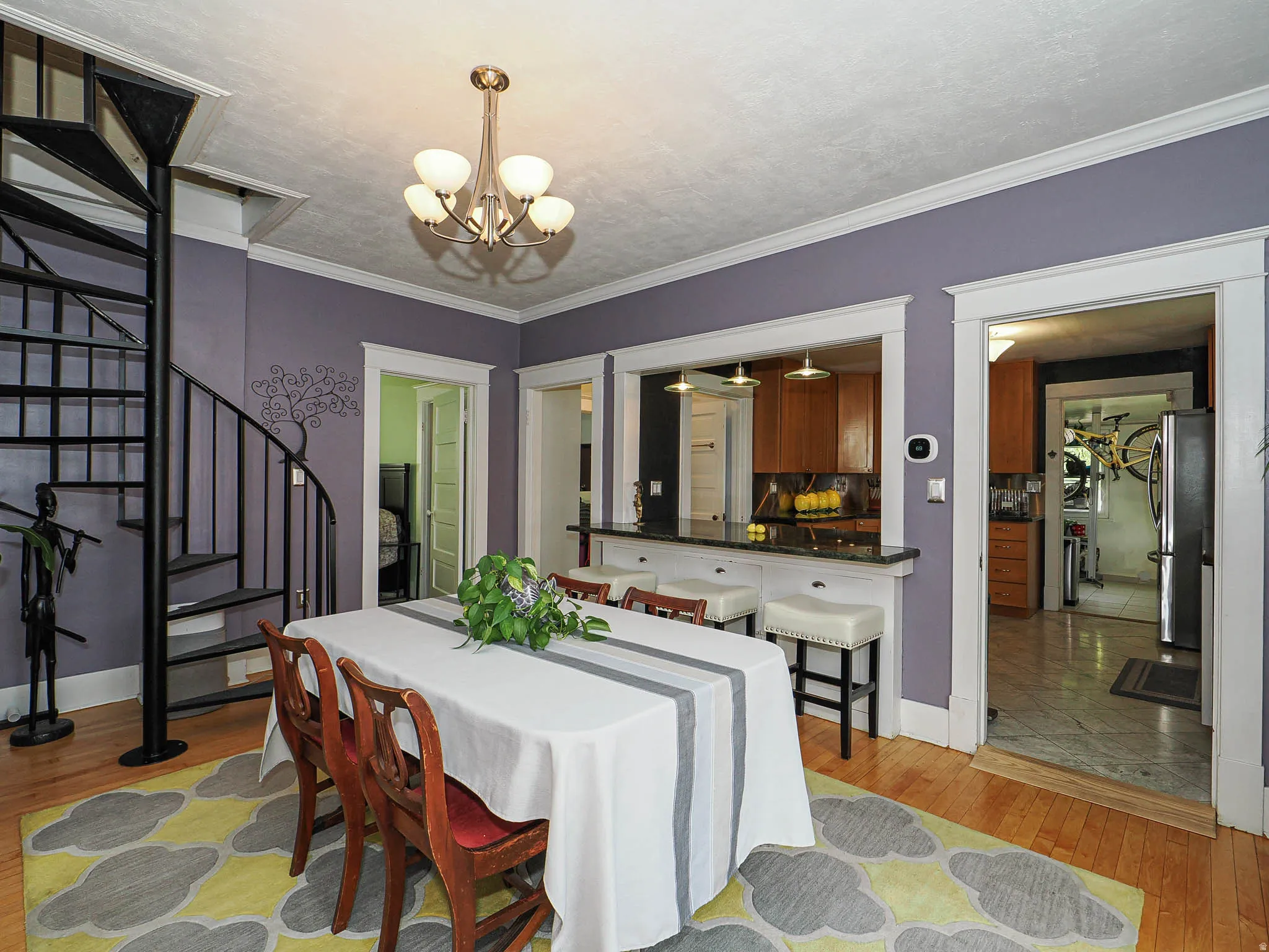 Hardwood flooring, spiral staircase with metal railing, built-in breakfast bar with stone countertop, wood-finish cabinetry, and overhead lighting fixture