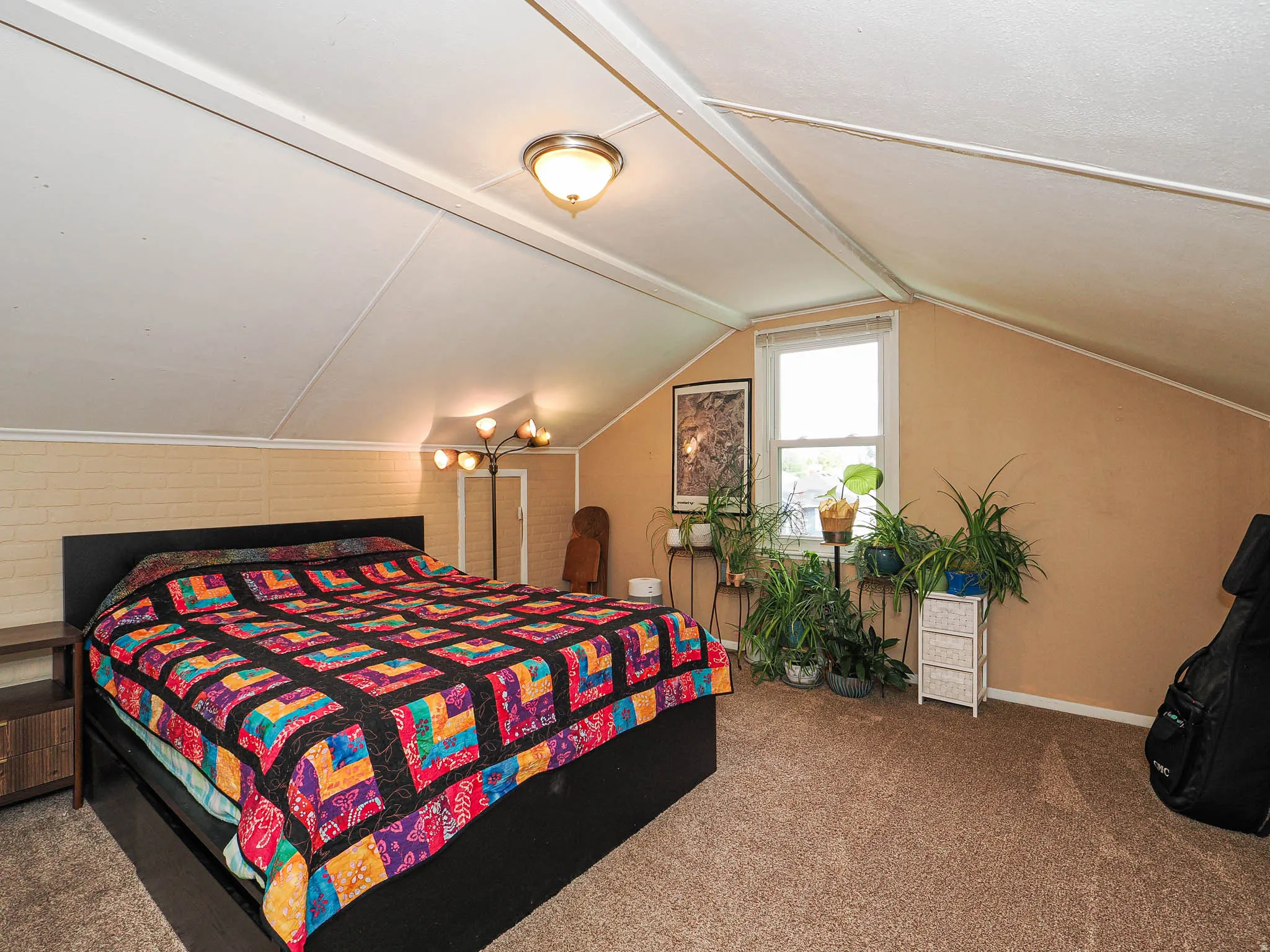 Sloped ceiling room featuring a window with natural light, textured wall finish, and a ceiling-mounted light fixture