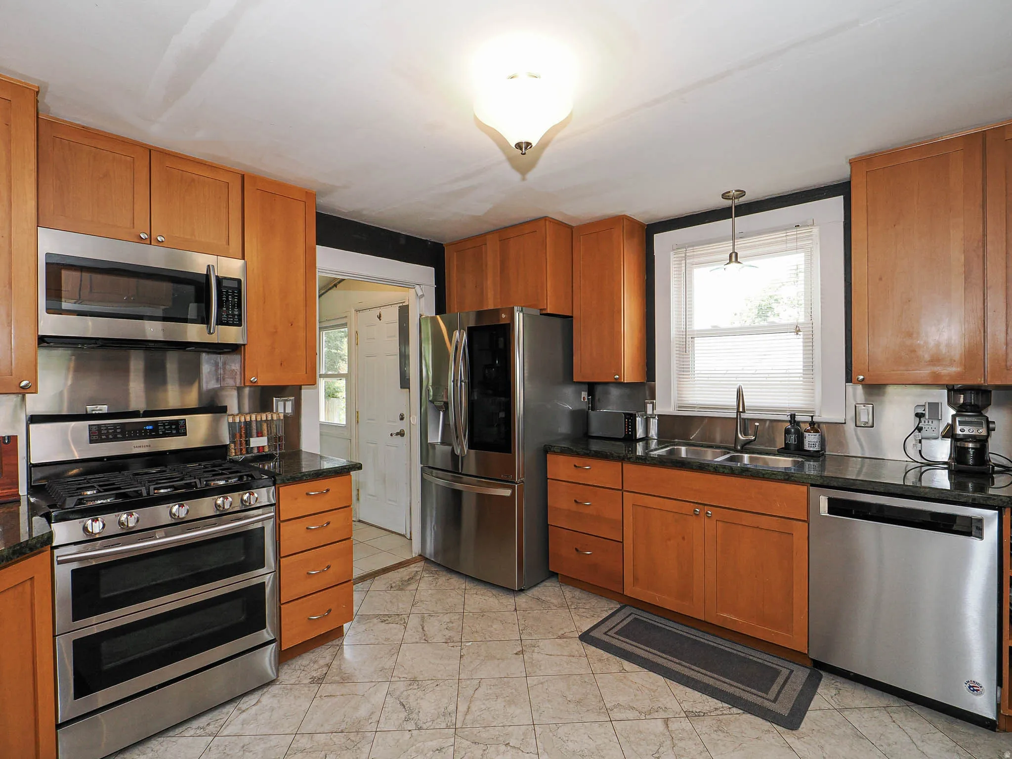 Kitchen featuring wood cabinetry, stainless steel appliances, dark countertops, and tiled flooring