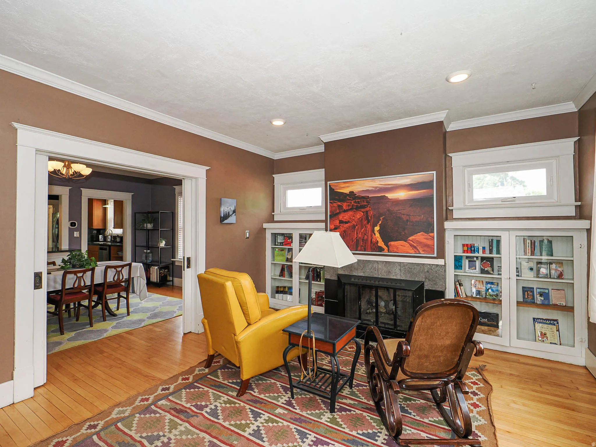 Hardwood flooring, crown molding, built-in shelving, windows with trim, and a fireplace with stone surround