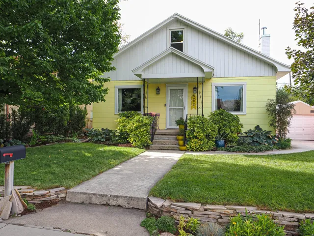Front elevation with yellow siding, a white gable roof, a concrete walkway, and landscaped garden beds