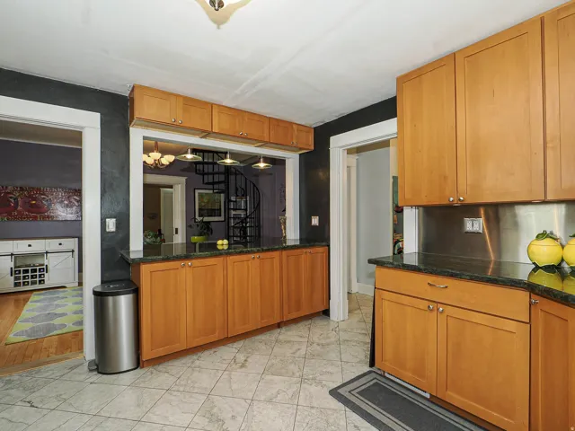 Kitchen featuring wood-finish cabinetry, dark countertops, tiled flooring, and a stainless steel backsplash