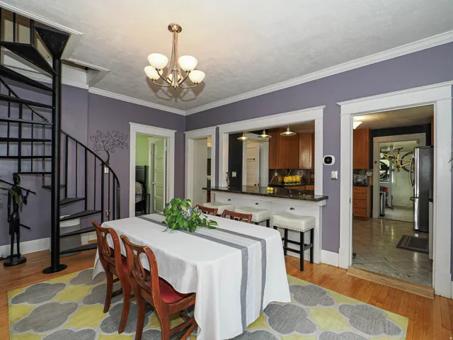 Hardwood flooring, spiral staircase with metal railing, built-in breakfast bar with stone countertop, wood-finish cabinetry, and overhead lighting fixture