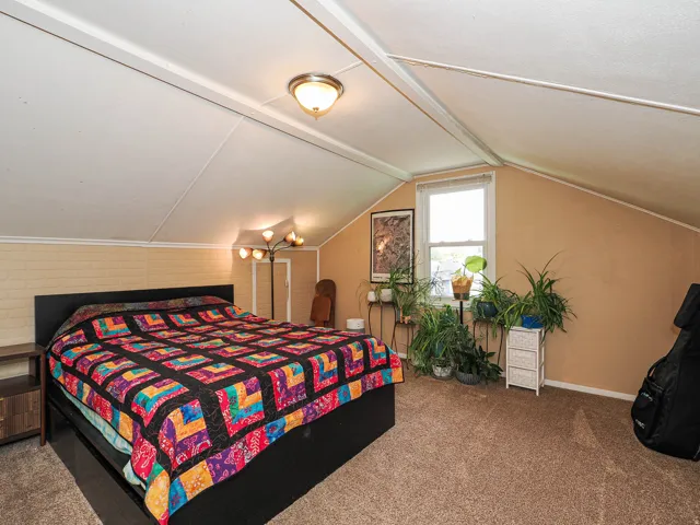 Sloped ceiling room featuring a window with natural light, textured wall finish, and a ceiling-mounted light fixture