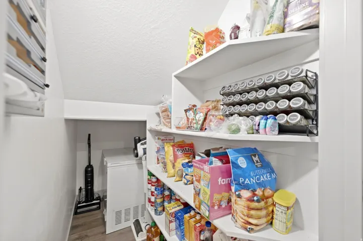 Walk-in pantry featuring white shelving, wood-finish flooring, and additional storage space