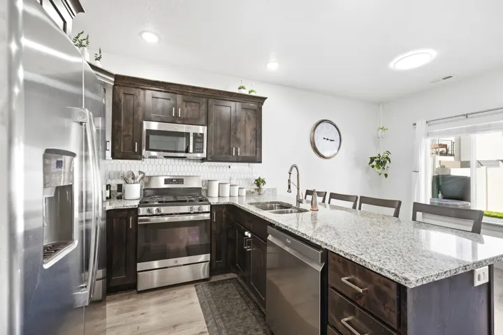 Kitchen featuring stainless steel appliances, dark wood-finish cabinetry, light-toned countertops, a tile backsplash, and a skylight