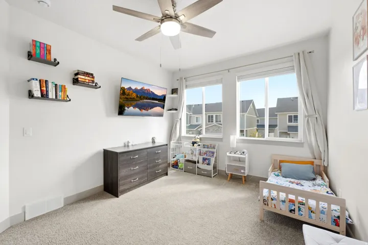Neutral wall paint, ceiling fan with integrated lighting, two large windows, and carpet flooring