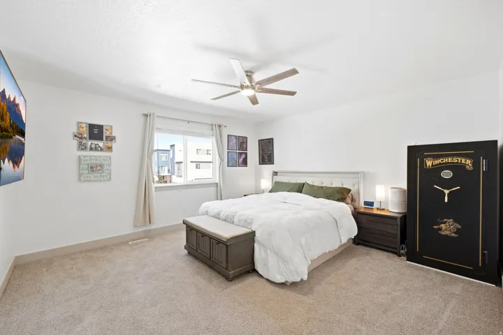 White walls with textured ceilings, light tan carpet, window with exterior view, and ceiling fan with integrated lighting