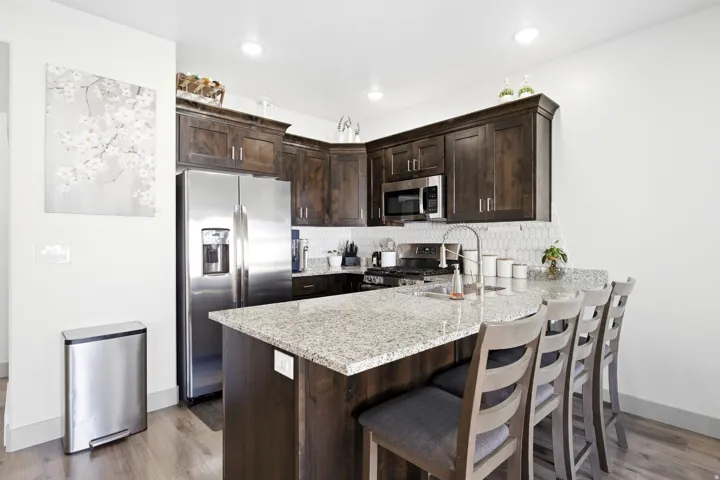 Kitchen featuring dark wood cabinetry, stainless steel appliances, granite countertops, a tile backsplash, and wood-finish flooring