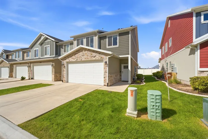 Two-story townhome featuring stone and siding exterior, an attached garage, a paved driveway, and a front entry door