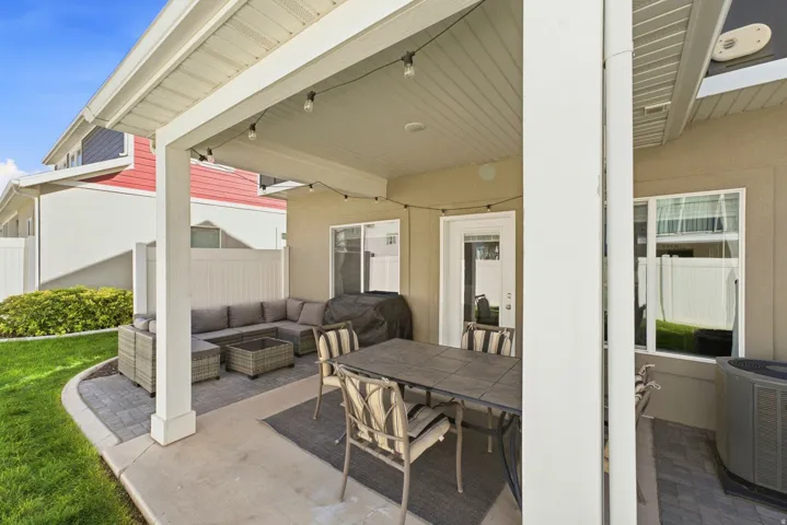 Covered patio with string lights, concrete flooring, and an adjacent paver stone patio