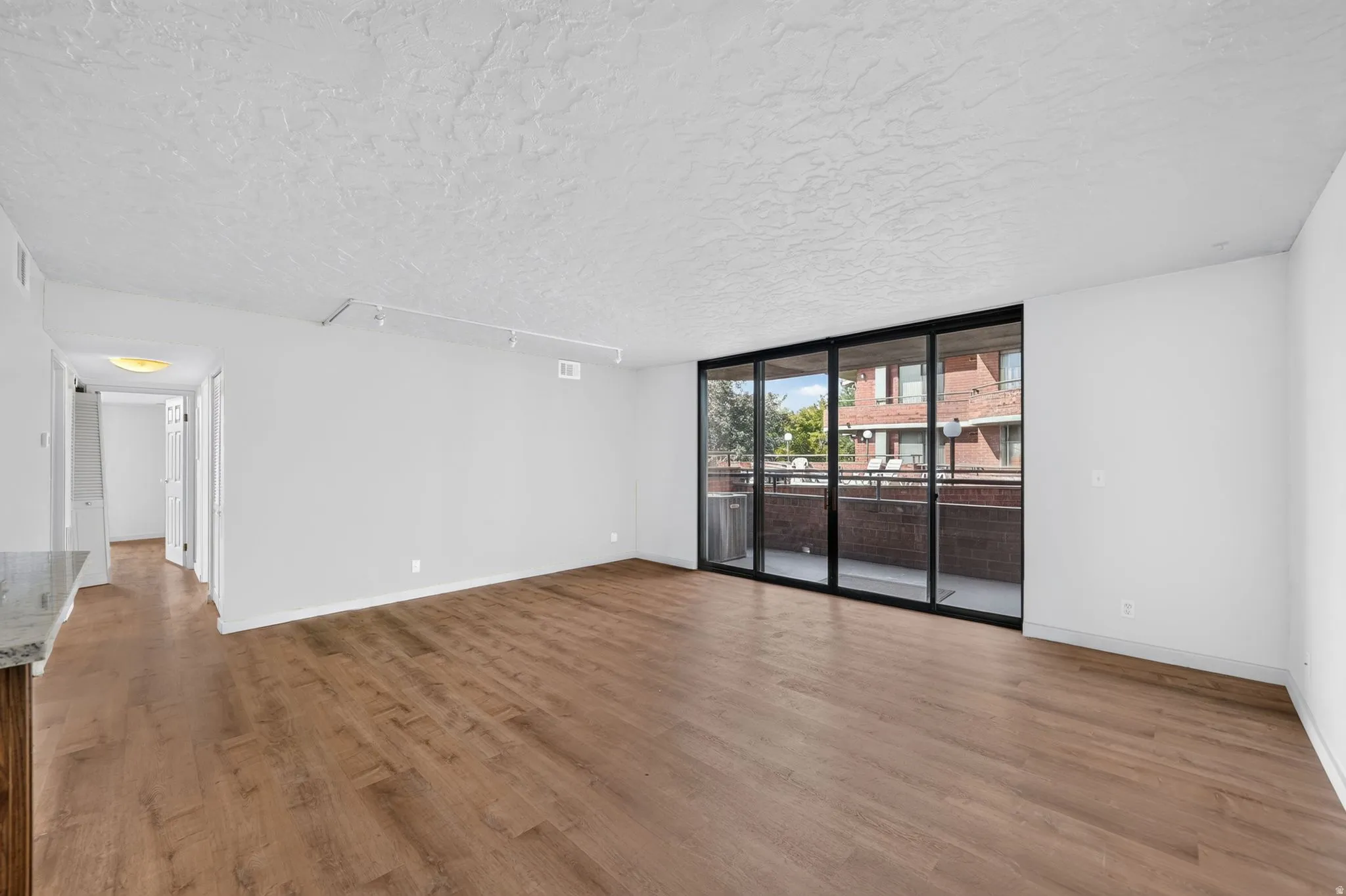 Spacious living area featuring wood-finish flooring, a full wall of sliding glass doors leading to a private balcony, and track lighting