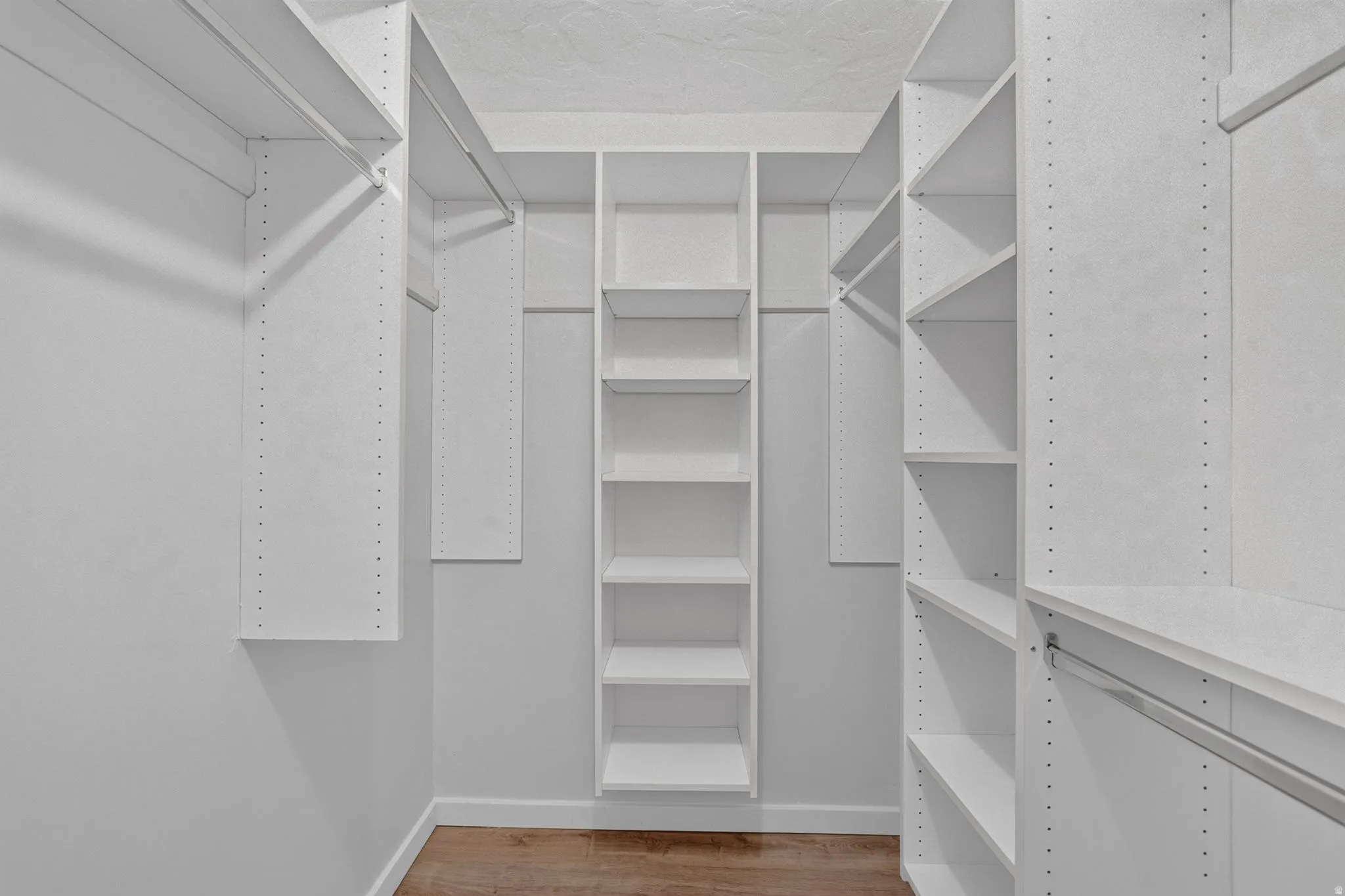 Built-in shelving, multiple hanging rods, and wood-finish flooring