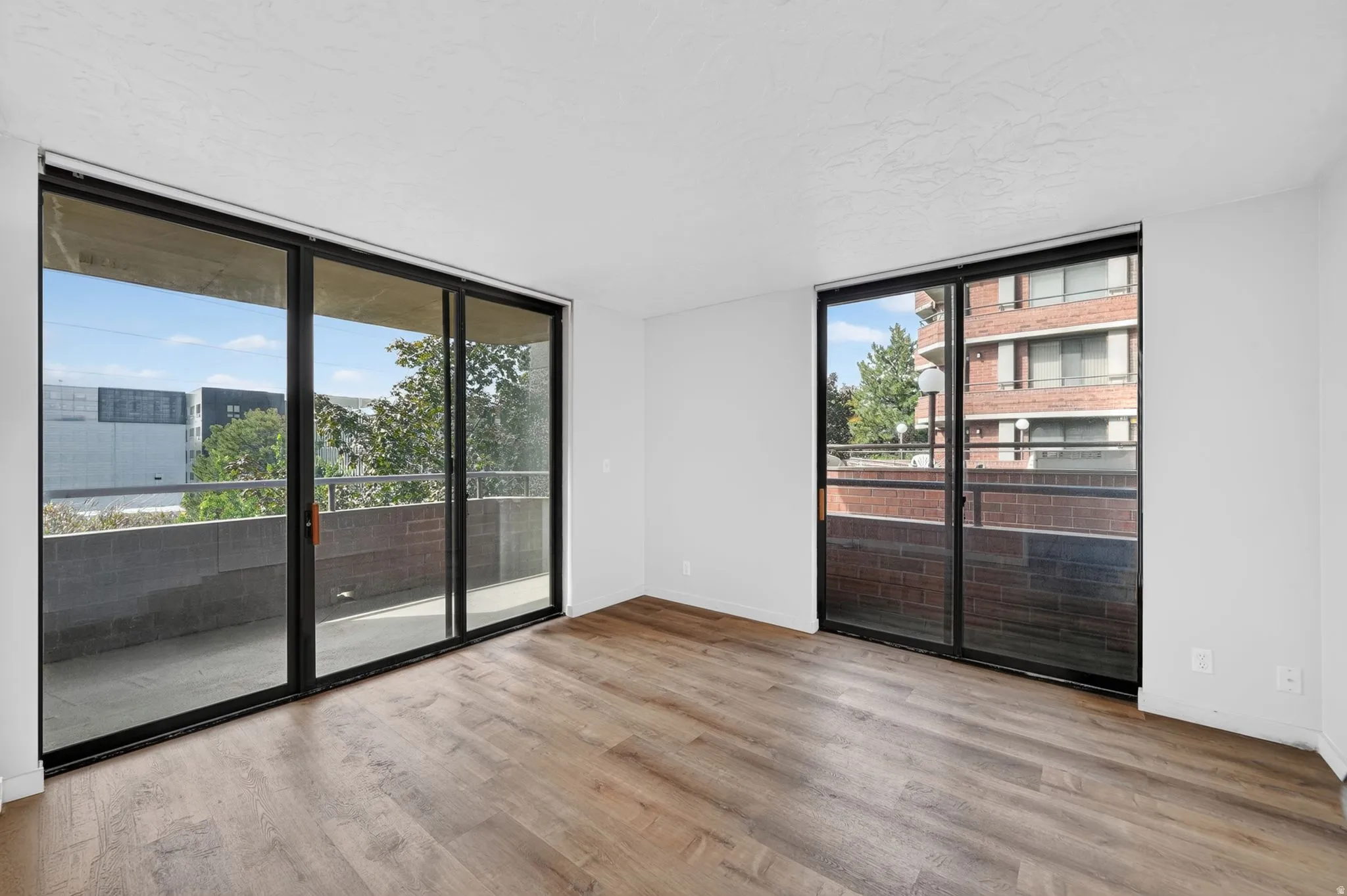 Expansive wood-finish flooring, white walls, a large sliding glass door to a balcony, and an additional sliding glass door
