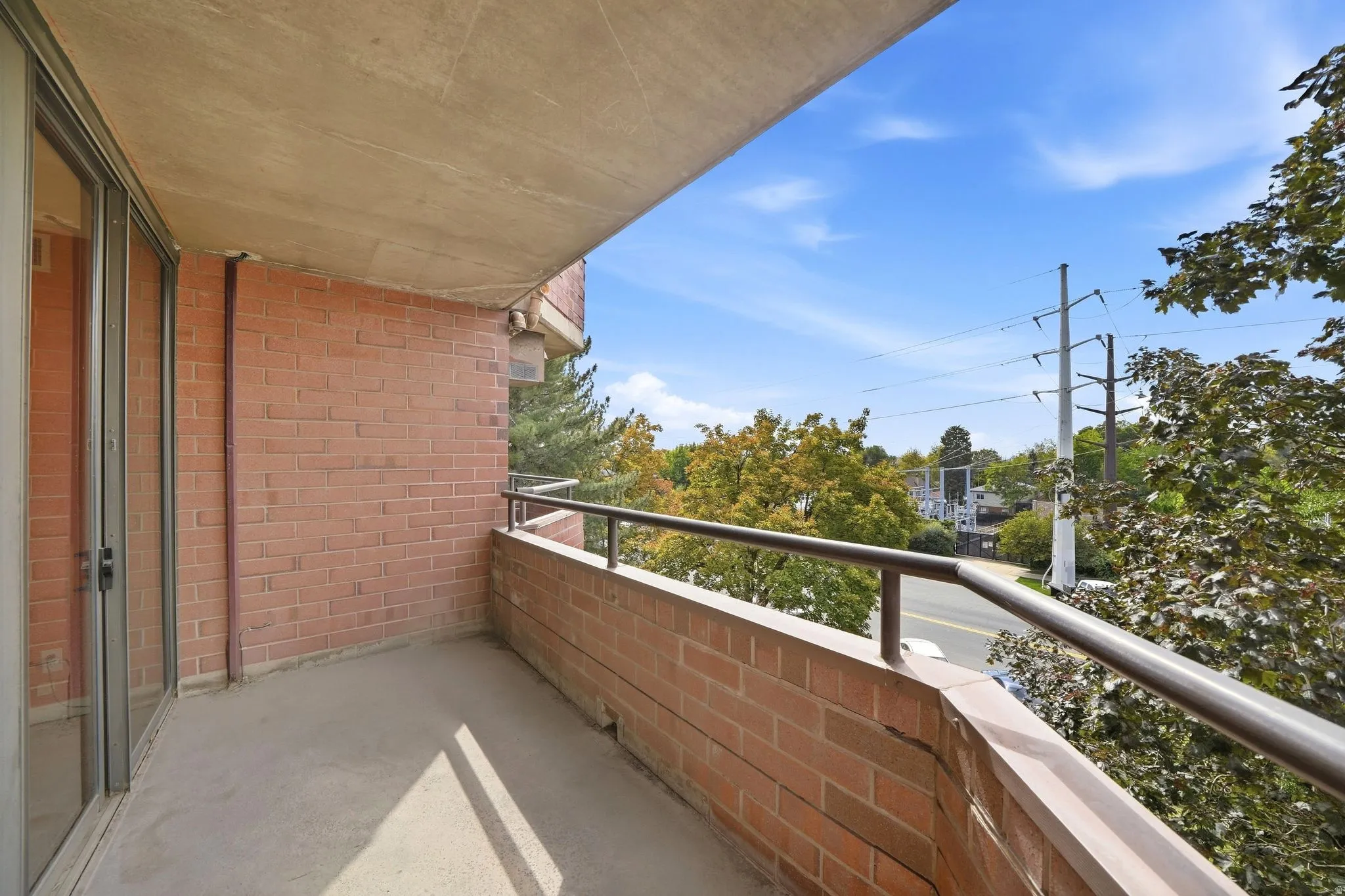 Private balcony with a brick facade, concrete flooring, and metal railing