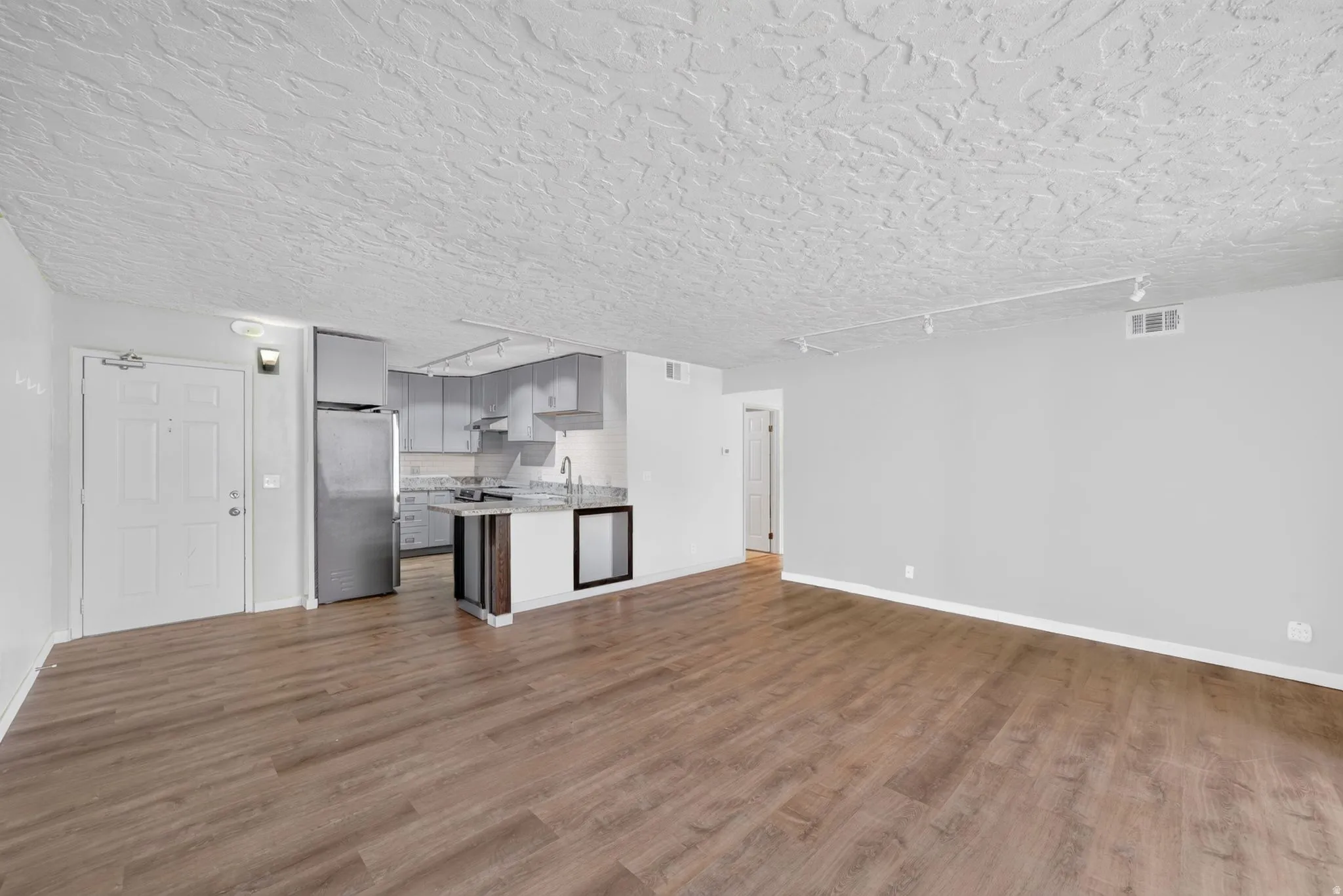 Wood-finish flooring throughout, kitchen with stainless steel appliances, grey cabinetry, and stone countertops, built-in beverage cooler, and track lighting