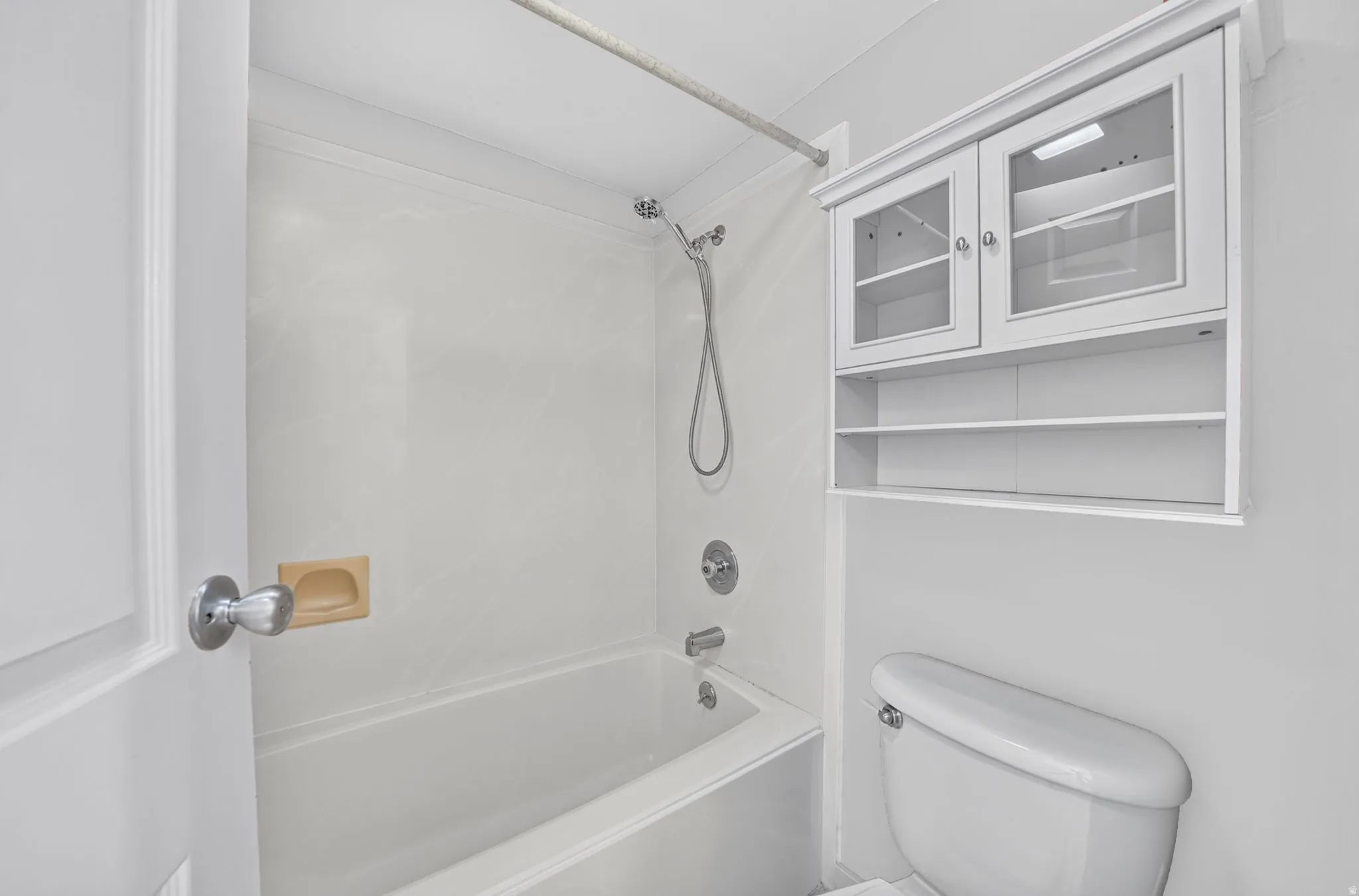 Bathtub with shower fixture, wall-mounted storage cabinet with glass inserts, and white toilet