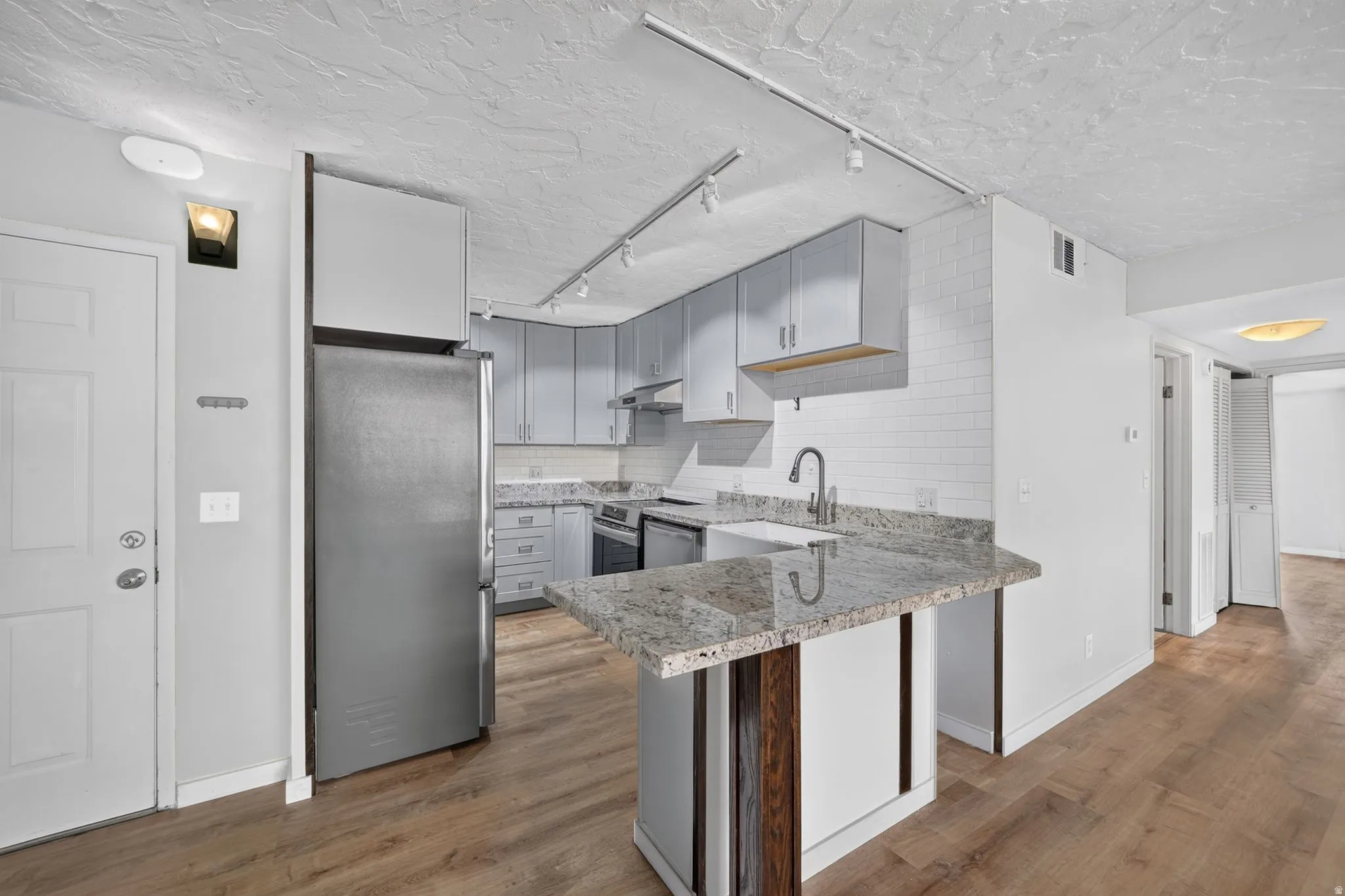Kitchen featuring stainless steel appliances, light gray cabinetry, a white subway tile backsplash, granite countertops, and wood-finish flooring