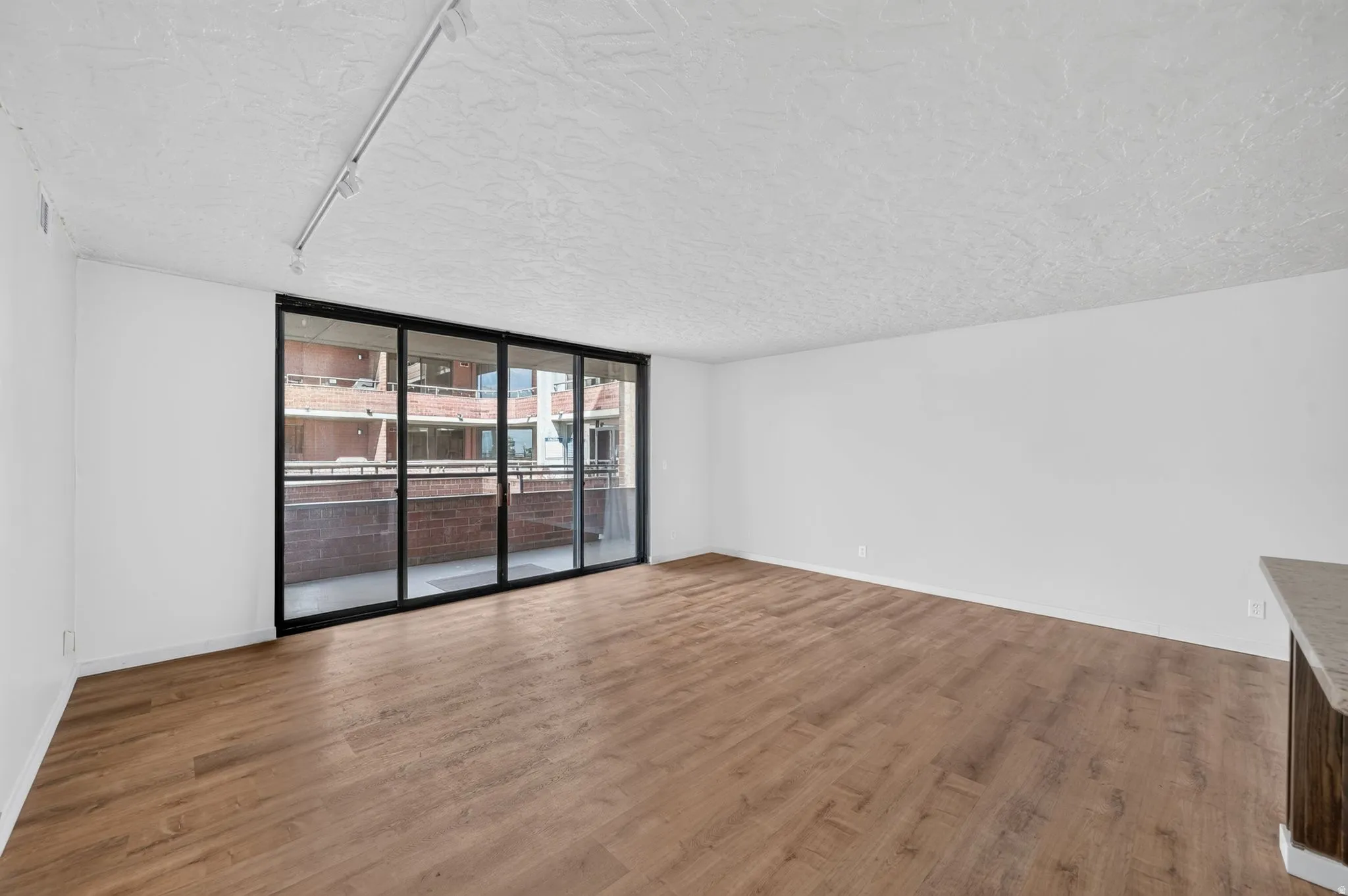 Wood-finish flooring, white walls, textured ceiling, track lighting, and a full-wall glass door
