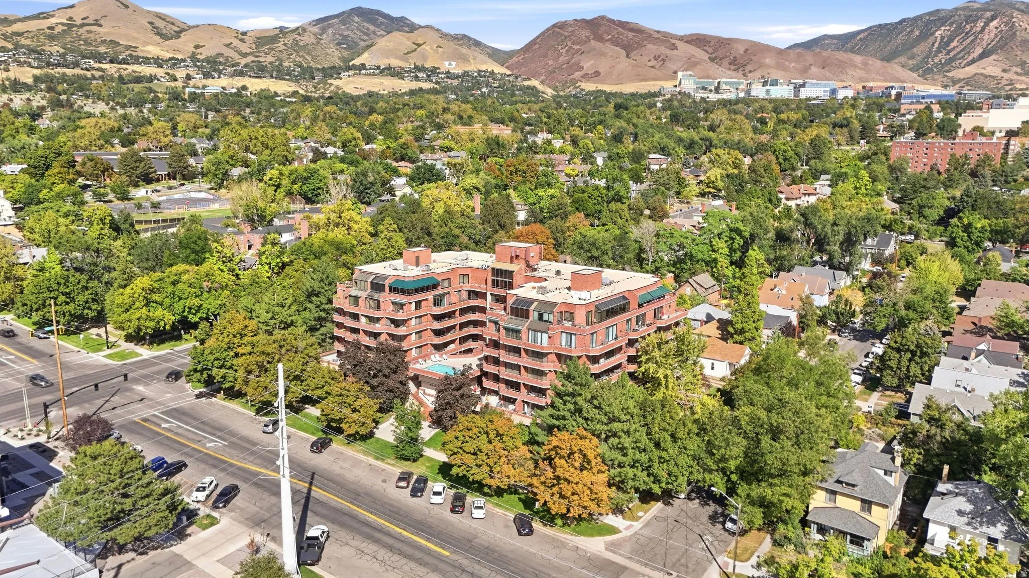 Multi-story brick building featuring balconies, flat roof with a green canopy, and surrounding mature trees